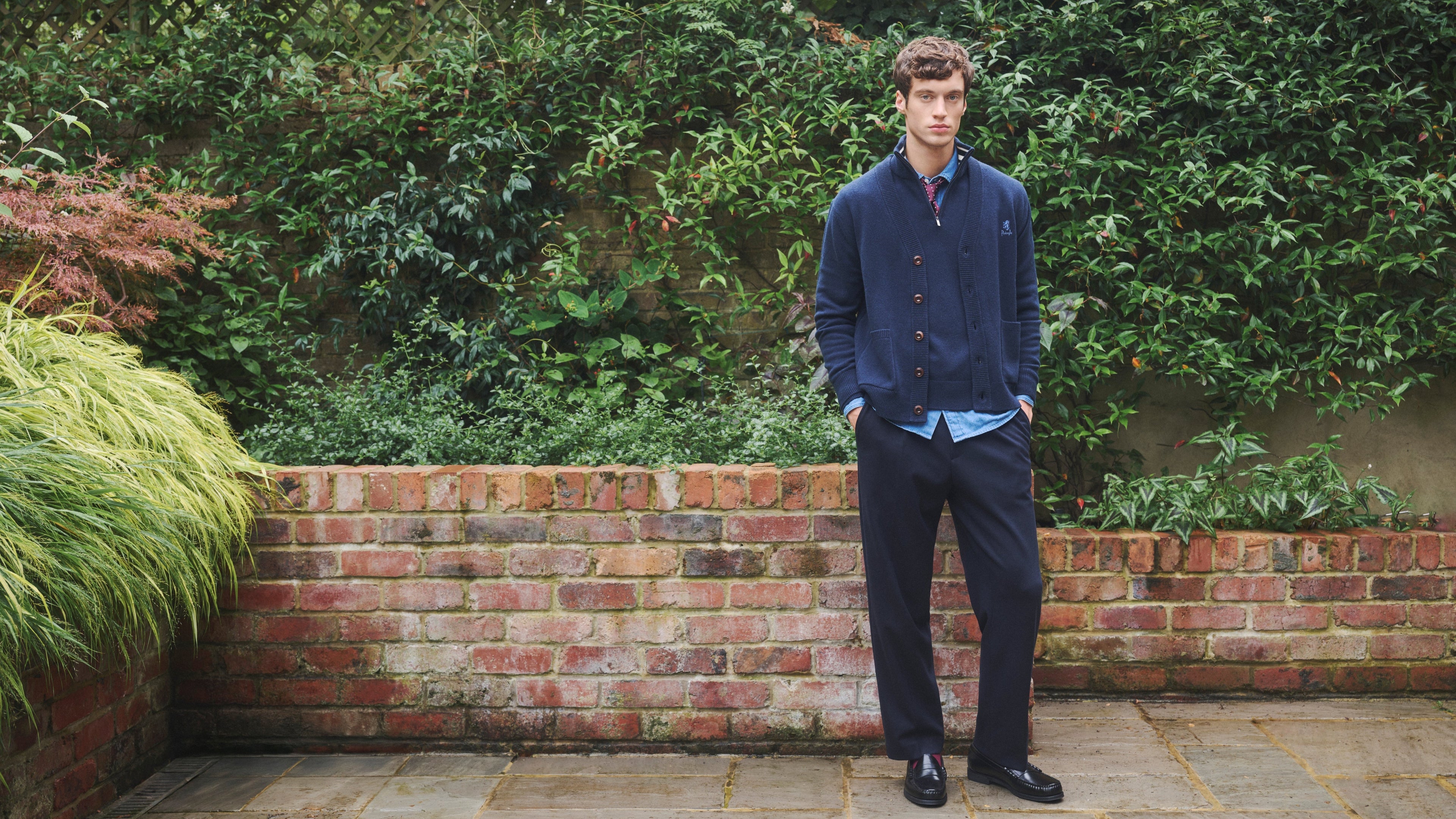 Man standing in a garden wearing a blue Pringle of Scotland cardigan