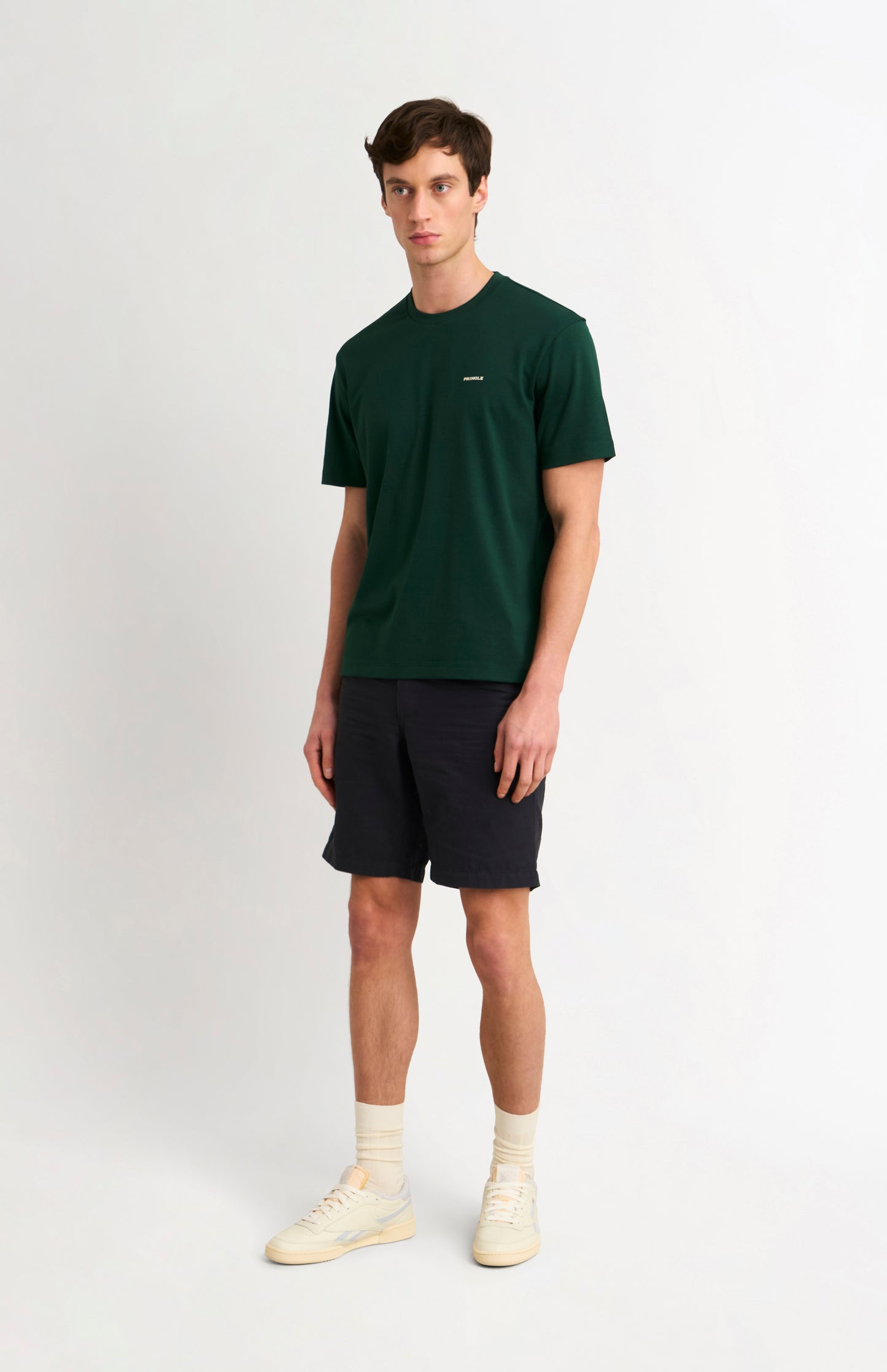 man wearing a dark green t-shirt and black shorts on a white background