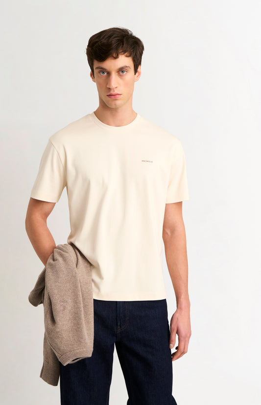 Man wearing an ecru t-shirt and dark jeans on a white background