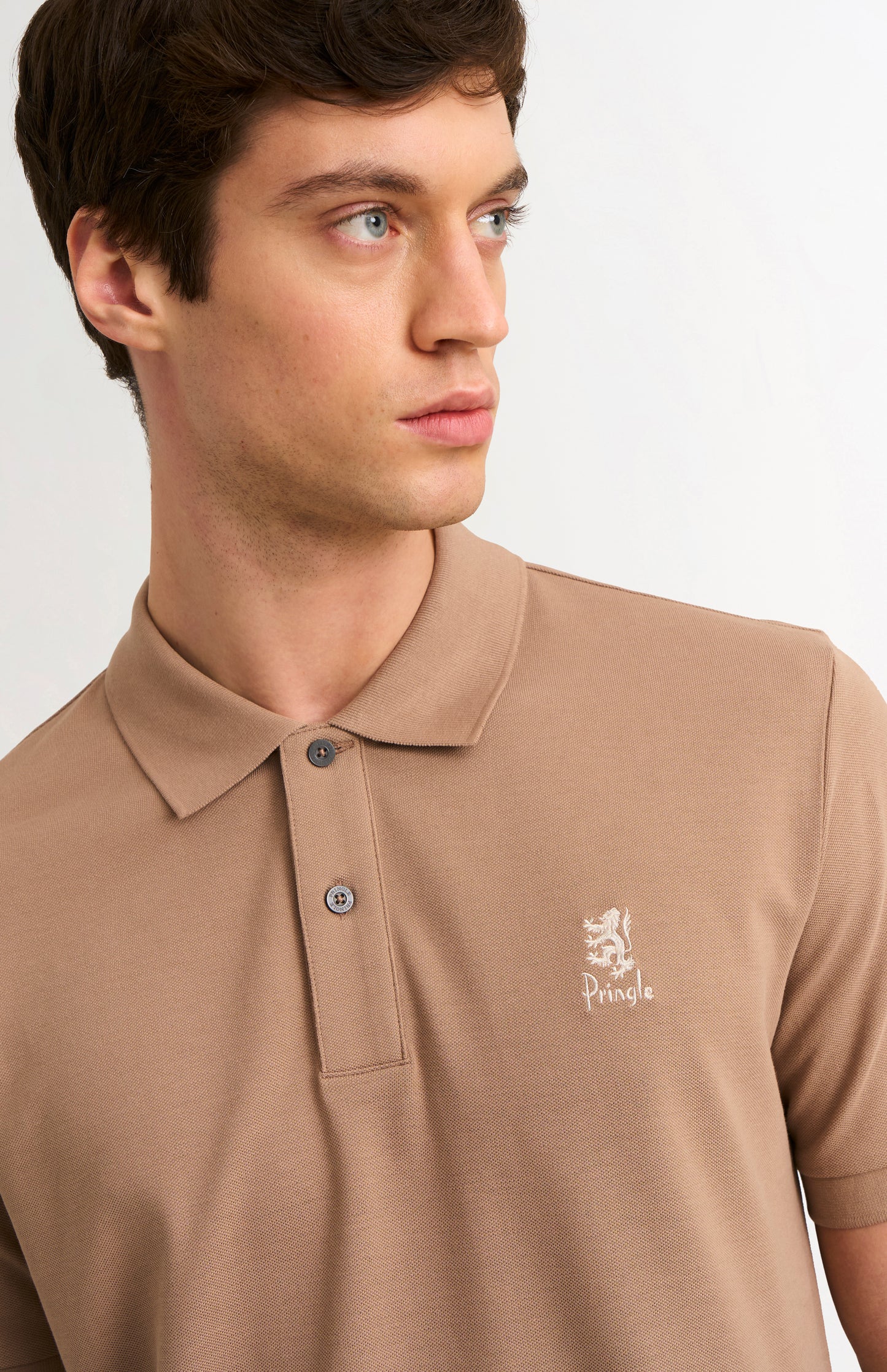Man wearing a brown polo shirt with a logo on a plain background