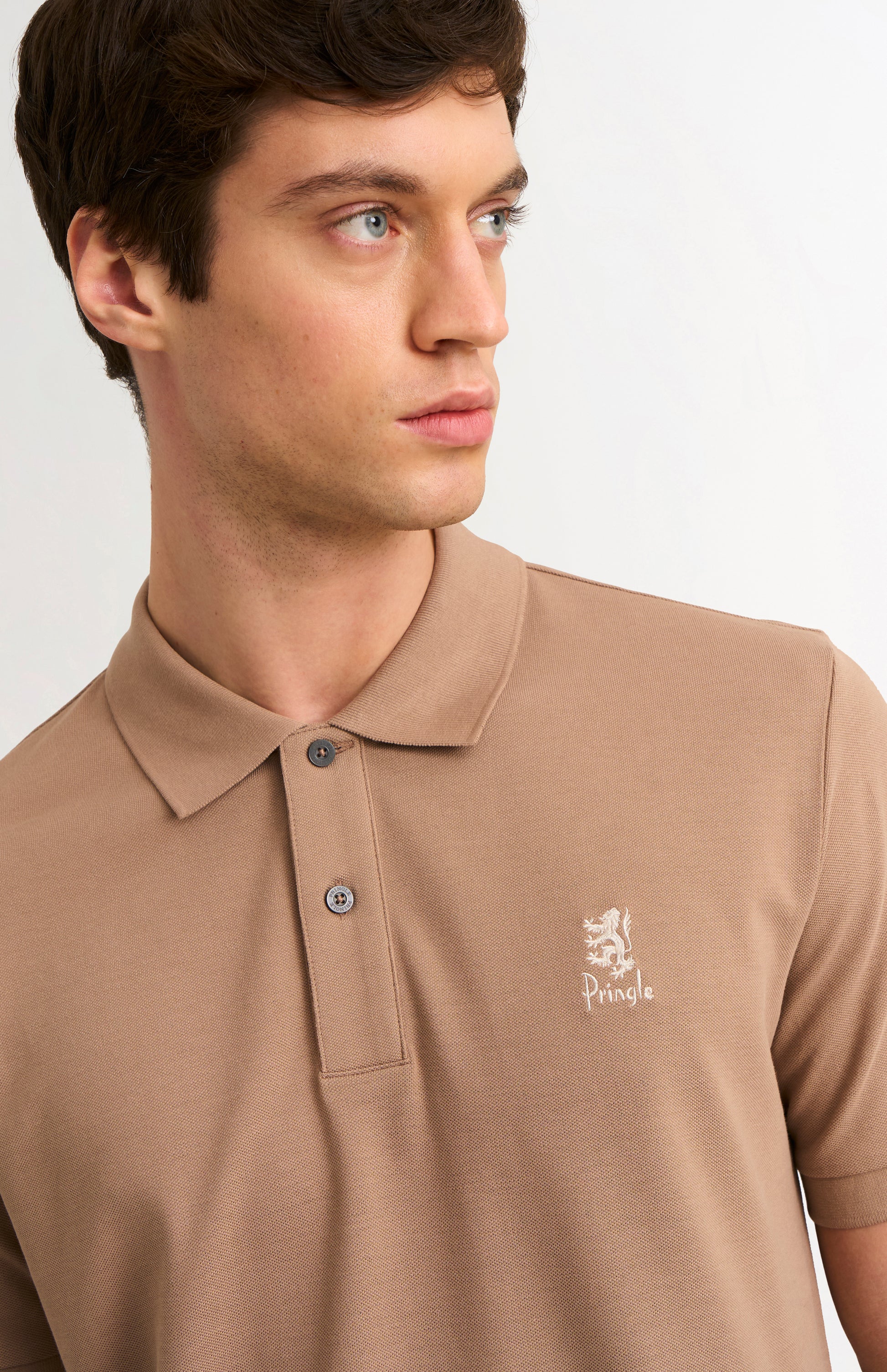 Man wearing a brown polo shirt with a logo on a plain background