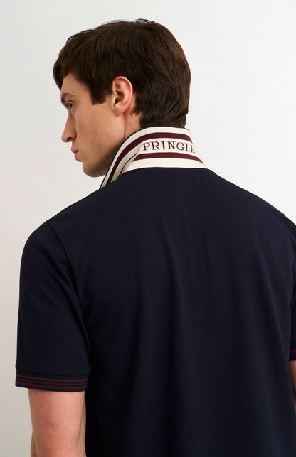 Detail shot of model wearing a navy polo shirt with burgundy tipping details and Pringle written under flipped-up collar