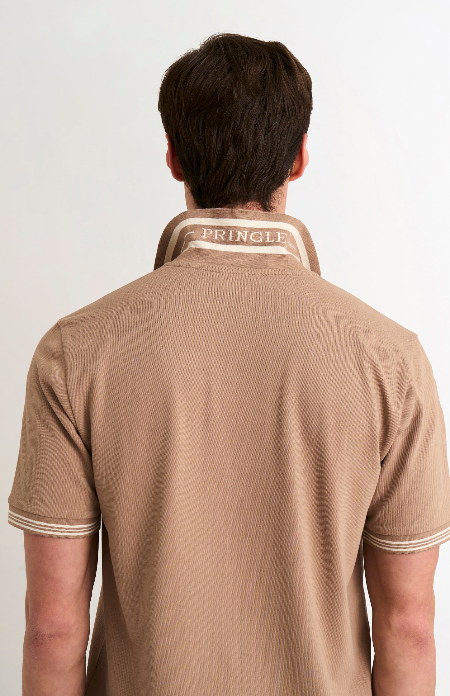 Model wearing a mushroom light brown polo with tipping and PRINGLE written under the flipped-up collar