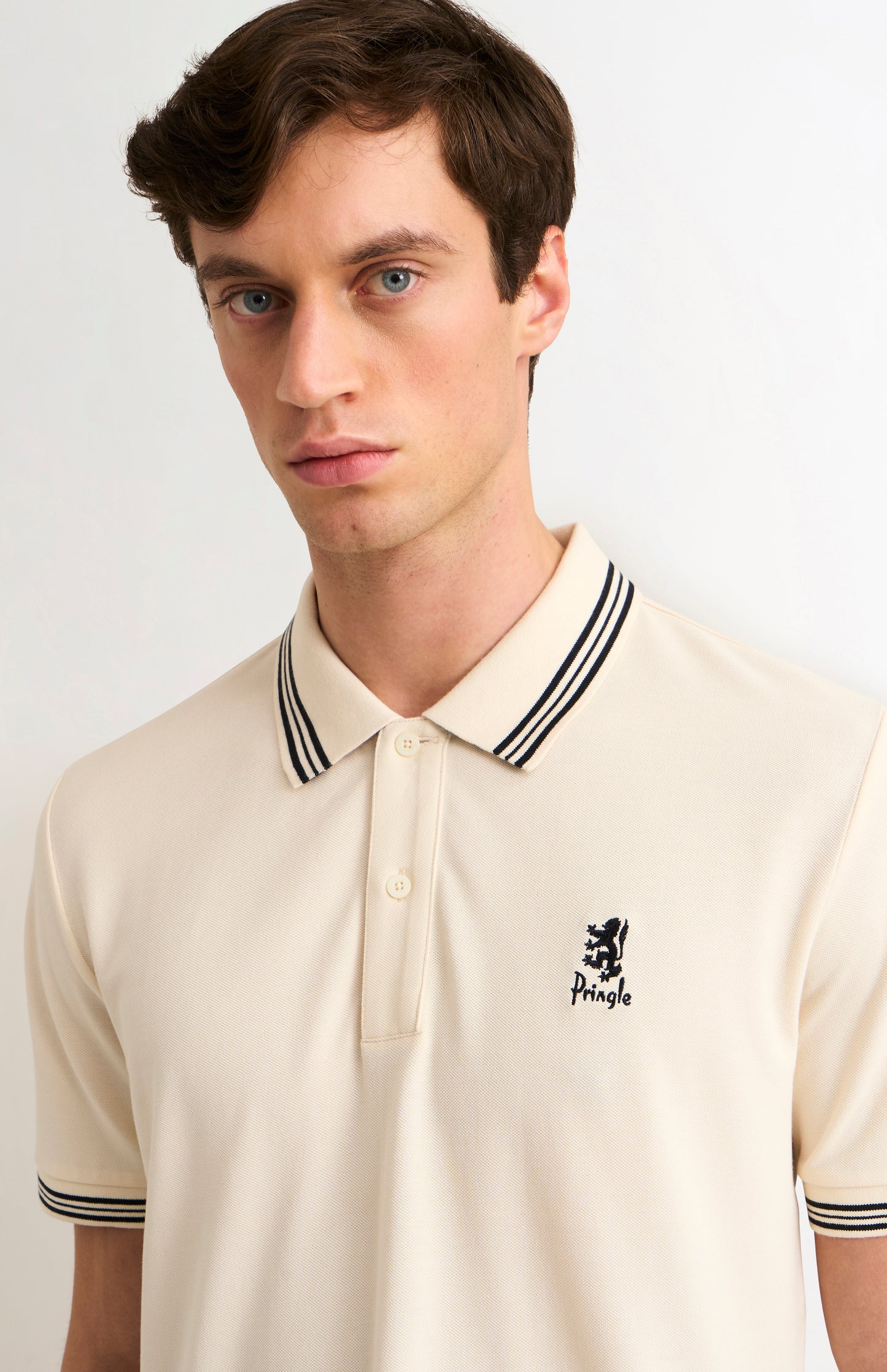 Man wearing a beige polo shirt with black and white trim on a light background