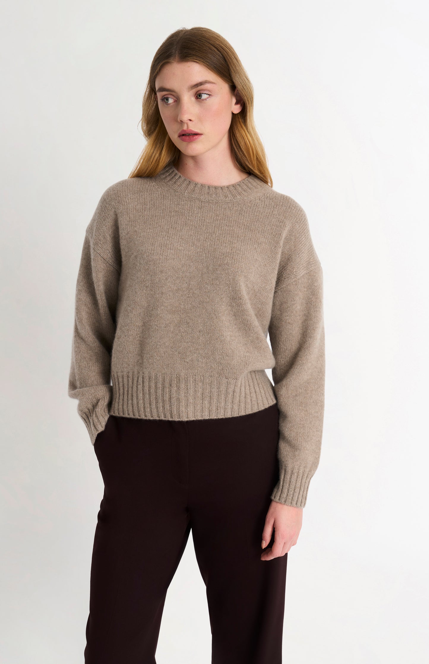 Woman wearing a beige sweater and black pants on a white background